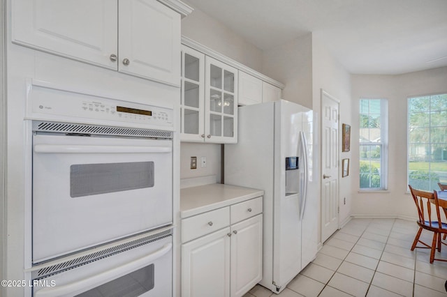 kitchen featuring glass insert cabinets, light countertops, light tile patterned flooring, white cabinets, and white appliances