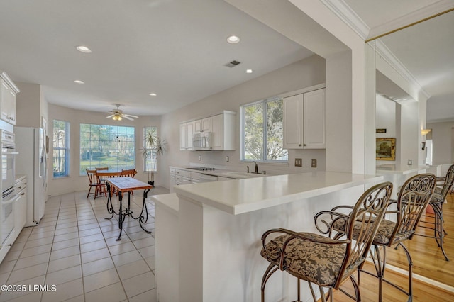 kitchen featuring white appliances, a peninsula, a sink, light countertops, and a kitchen bar