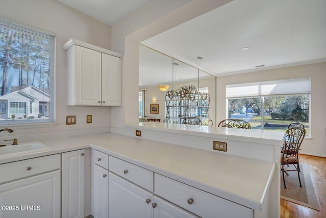 kitchen with light wood finished floors, light countertops, a peninsula, white cabinetry, and a sink