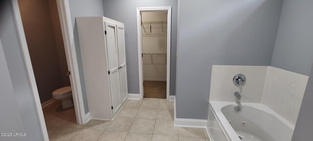 bathroom with tile patterned floors, a walk in closet, toilet, baseboards, and a bath