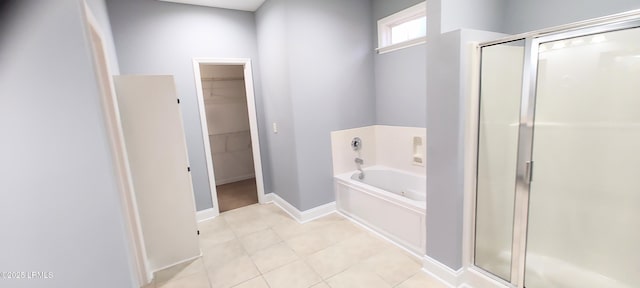 bathroom featuring a walk in closet, a garden tub, a shower stall, tile patterned flooring, and baseboards