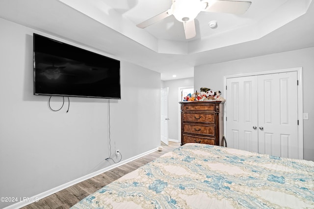 bedroom featuring a raised ceiling, light hardwood / wood-style flooring, ceiling fan, and a closet