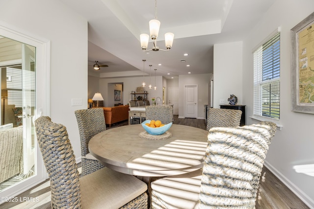 dining area with baseboards, wood finished floors, ceiling fan with notable chandelier, and a tray ceiling