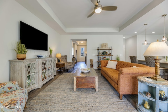 living room featuring a ceiling fan, a tray ceiling, recessed lighting, and wood finished floors