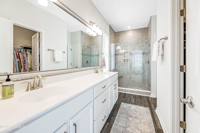 full bath featuring a sink, a walk in closet, a stall shower, and wood finished floors