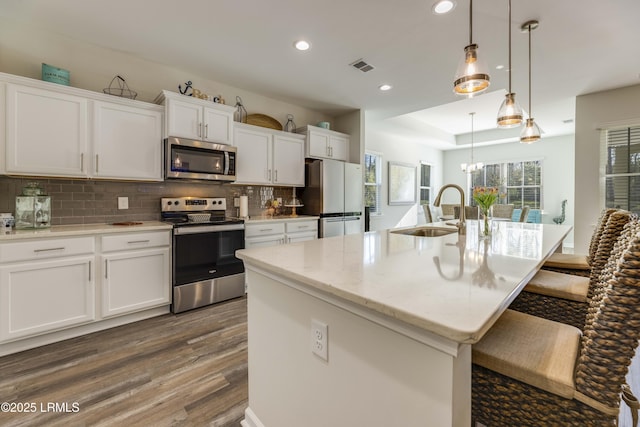 kitchen with visible vents, appliances with stainless steel finishes, tasteful backsplash, wood finished floors, and a sink