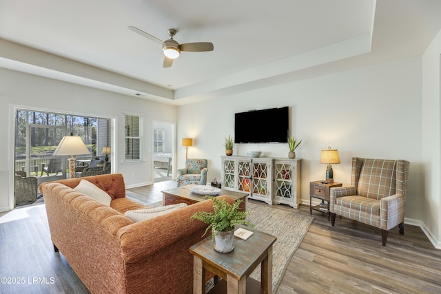living area with a raised ceiling, baseboards, a ceiling fan, and wood finished floors