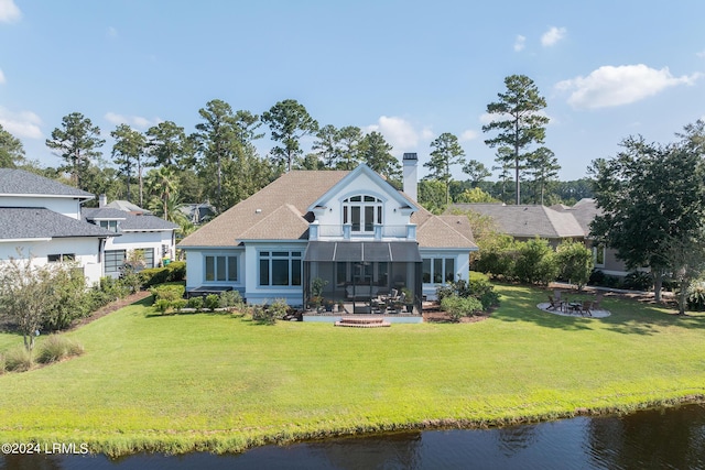 back of property with an outdoor fire pit, a lawn, a balcony, and a water view