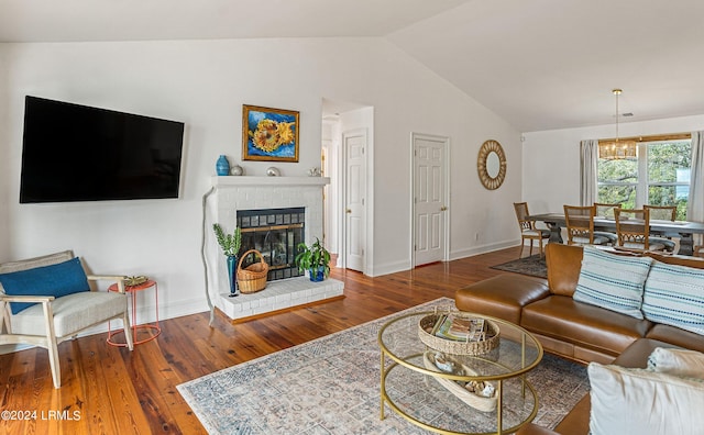 living room featuring dark wood-type flooring, an inviting chandelier, vaulted ceiling, and a brick fireplace