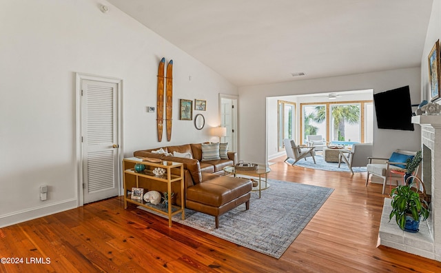 living room with hardwood / wood-style flooring, lofted ceiling, and a brick fireplace