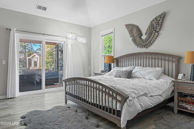 bedroom with wood-type flooring, vaulted ceiling, multiple windows, and access to outside