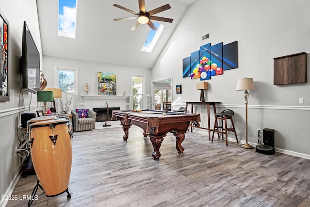 recreation room with a tiled fireplace, a healthy amount of sunlight, hardwood / wood-style floors, and a skylight