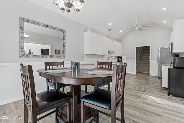 dining space featuring vaulted ceiling, sink, ceiling fan with notable chandelier, and light hardwood / wood-style flooring