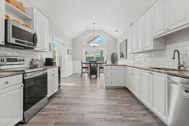 kitchen with vaulted ceiling, appliances with stainless steel finishes, sink, white cabinets, and hanging light fixtures