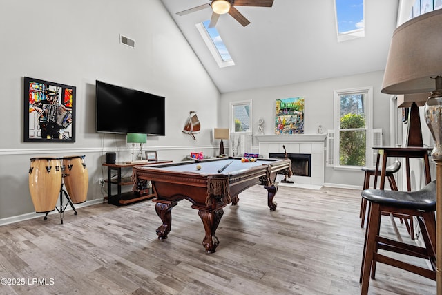 game room with a fireplace, a skylight, high vaulted ceiling, and light wood-type flooring