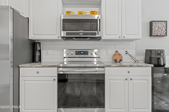 kitchen featuring stainless steel appliances, white cabinetry, light stone countertops, and decorative backsplash