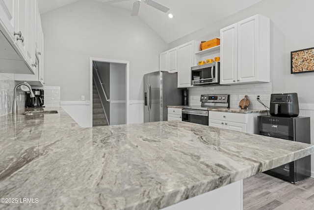 kitchen with ceiling fan, appliances with stainless steel finishes, white cabinetry, high vaulted ceiling, and light stone counters