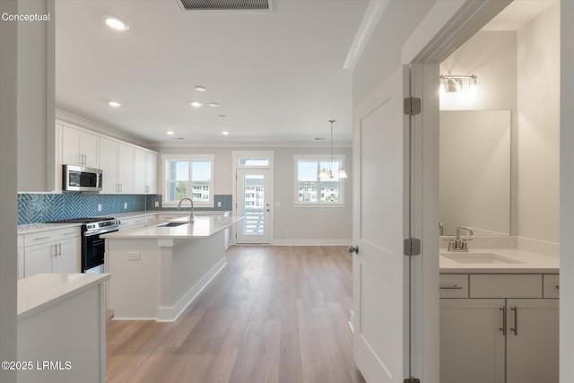 421 Parkside Commons, Bluffton, SC 29910 - kitchen with stainless steel appliances, light wood-type flooring, decorative backsplash, white cabinetry, and a center island with sink