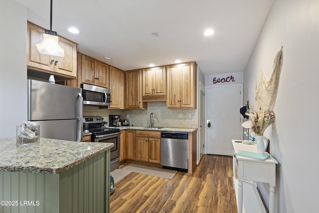 kitchen with sink, tasteful backsplash, hanging light fixtures, appliances with stainless steel finishes, and light stone countertops