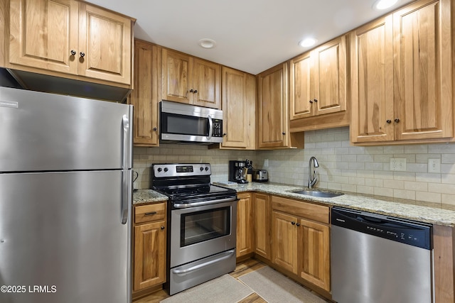 kitchen featuring appliances with stainless steel finishes, sink, light stone counters, and decorative backsplash