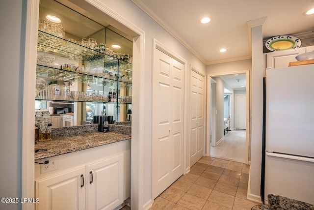 bar featuring white cabinetry, crown molding, dark stone counters, and white fridge