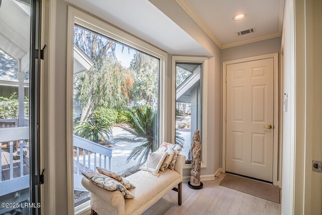 doorway with crown molding, a wealth of natural light, and light wood-type flooring