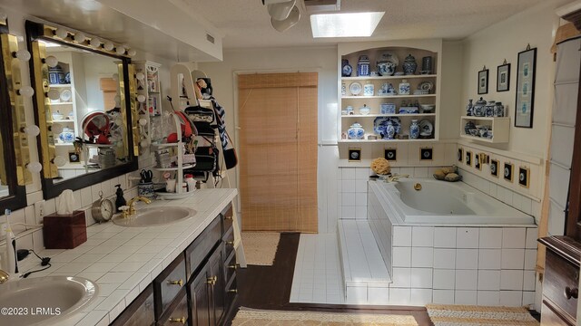 bathroom with a relaxing tiled tub, built in features, vanity, and a textured ceiling