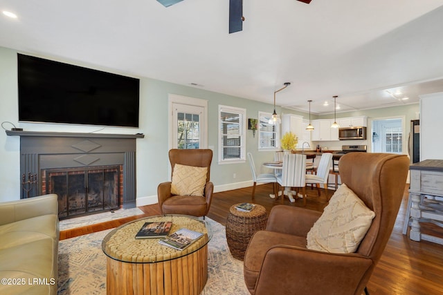 living area with a brick fireplace, plenty of natural light, baseboards, and wood finished floors