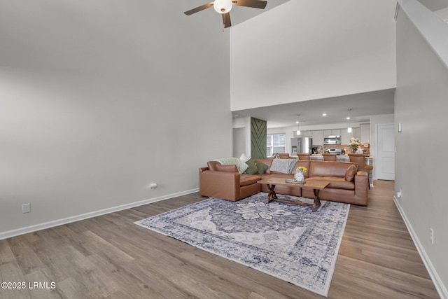 living room featuring light wood-style flooring, baseboards, and a towering ceiling