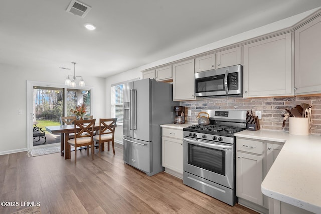 kitchen featuring visible vents, stainless steel appliances, hanging light fixtures, tasteful backsplash, and light wood-type flooring