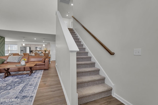 stairway with visible vents, baseboards, a high ceiling, and wood finished floors