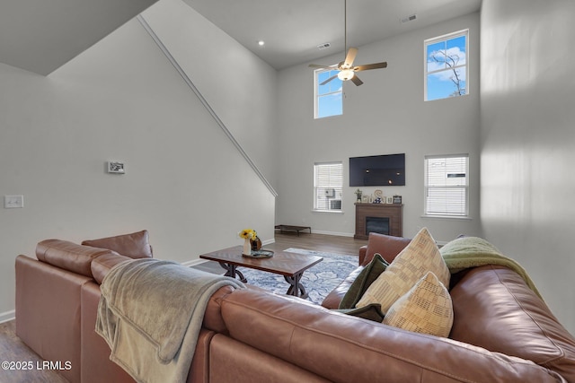 living area featuring wood finished floors, visible vents, baseboards, a fireplace, and ceiling fan