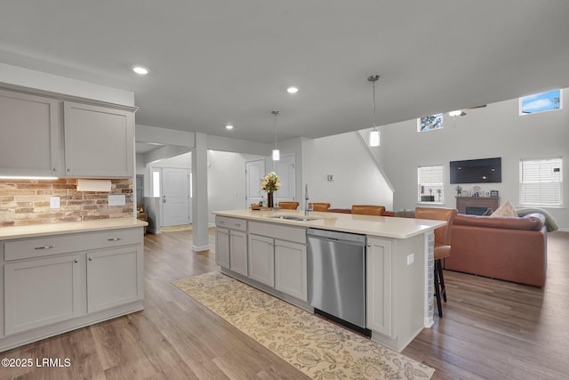 kitchen with light wood-style flooring, a sink, light countertops, stainless steel dishwasher, and open floor plan