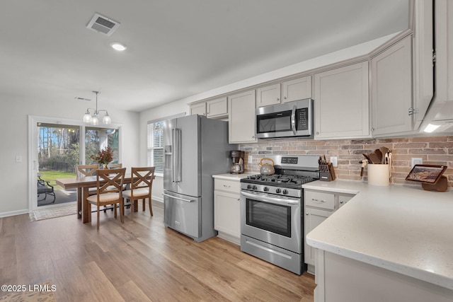 kitchen with light wood finished floors, visible vents, backsplash, pendant lighting, and appliances with stainless steel finishes