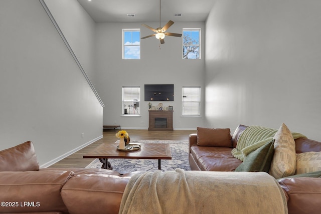 living room featuring visible vents, wood finished floors, a glass covered fireplace, baseboards, and ceiling fan