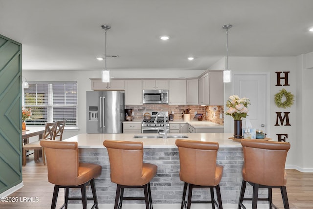 kitchen featuring light wood finished floors, a sink, stainless steel appliances, light countertops, and decorative backsplash