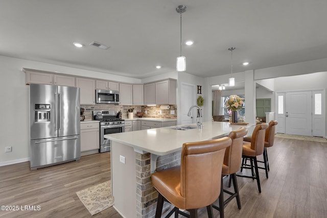 kitchen featuring visible vents, light wood-style flooring, a sink, stainless steel appliances, and decorative backsplash