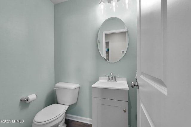 half bathroom with baseboards, toilet, and vanity