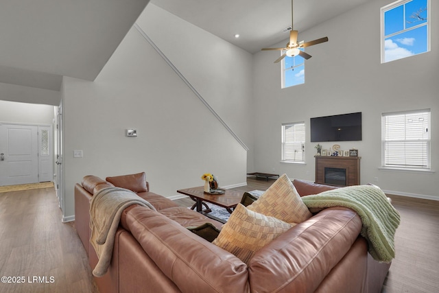 living area featuring a fireplace, a high ceiling, baseboards, and wood finished floors