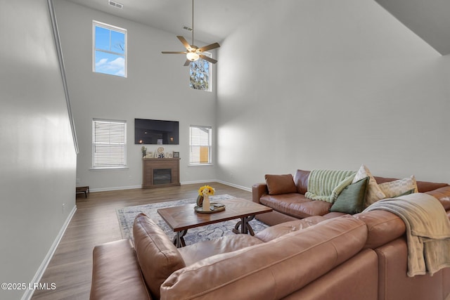 living room with visible vents, baseboards, ceiling fan, a fireplace, and wood finished floors