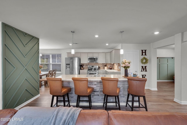 kitchen featuring backsplash, light countertops, appliances with stainless steel finishes, a kitchen breakfast bar, and a sink