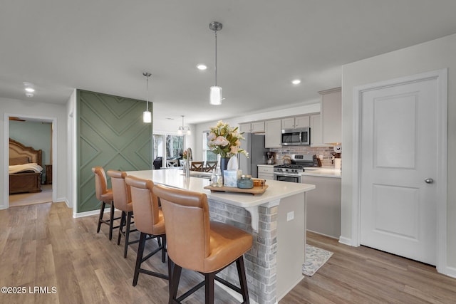 kitchen with a kitchen island with sink, light wood-style flooring, a kitchen breakfast bar, stainless steel appliances, and a sink