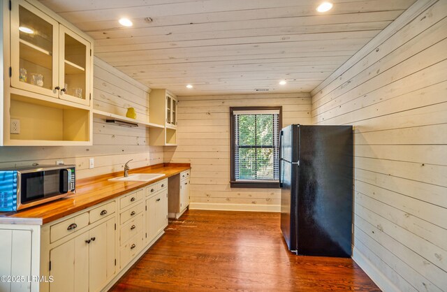 kitchen featuring black refrigerator, wood counters, wood walls, sink, and white cabinets