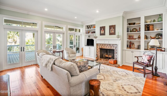 living room featuring built in features, ornamental molding, a brick fireplace, light wood-type flooring, and french doors