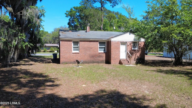 view of side of home featuring entry steps, a chimney, a lawn, and brick siding