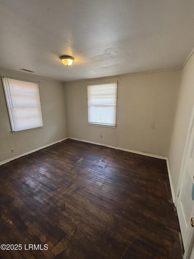 empty room with dark wood-style flooring, visible vents, and baseboards