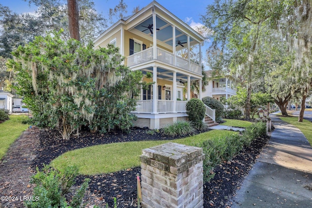 view of front facade featuring a front yard, a balcony, ceiling fan, and covered porch