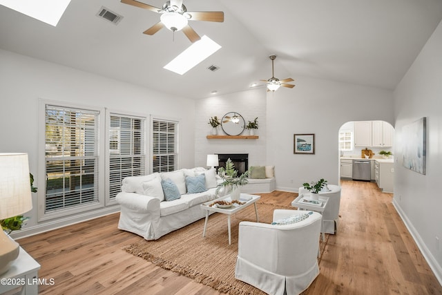 living room with light wood-type flooring, arched walkways, a brick fireplace, and visible vents