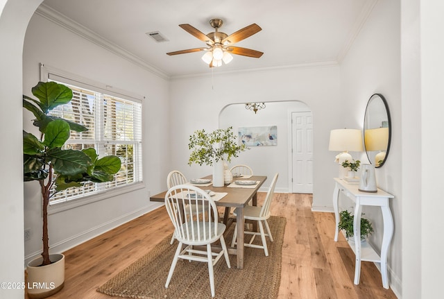 dining area featuring visible vents, arched walkways, light wood-style floors, crown molding, and baseboards