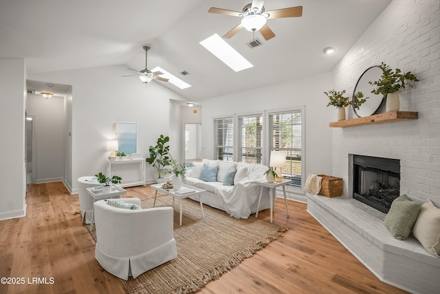 living area featuring light wood-style flooring, a brick fireplace, a skylight, and visible vents